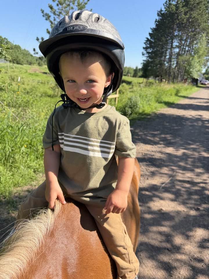 A smiling child in a riding helmet sits on a pony at Full Circle Vaulting