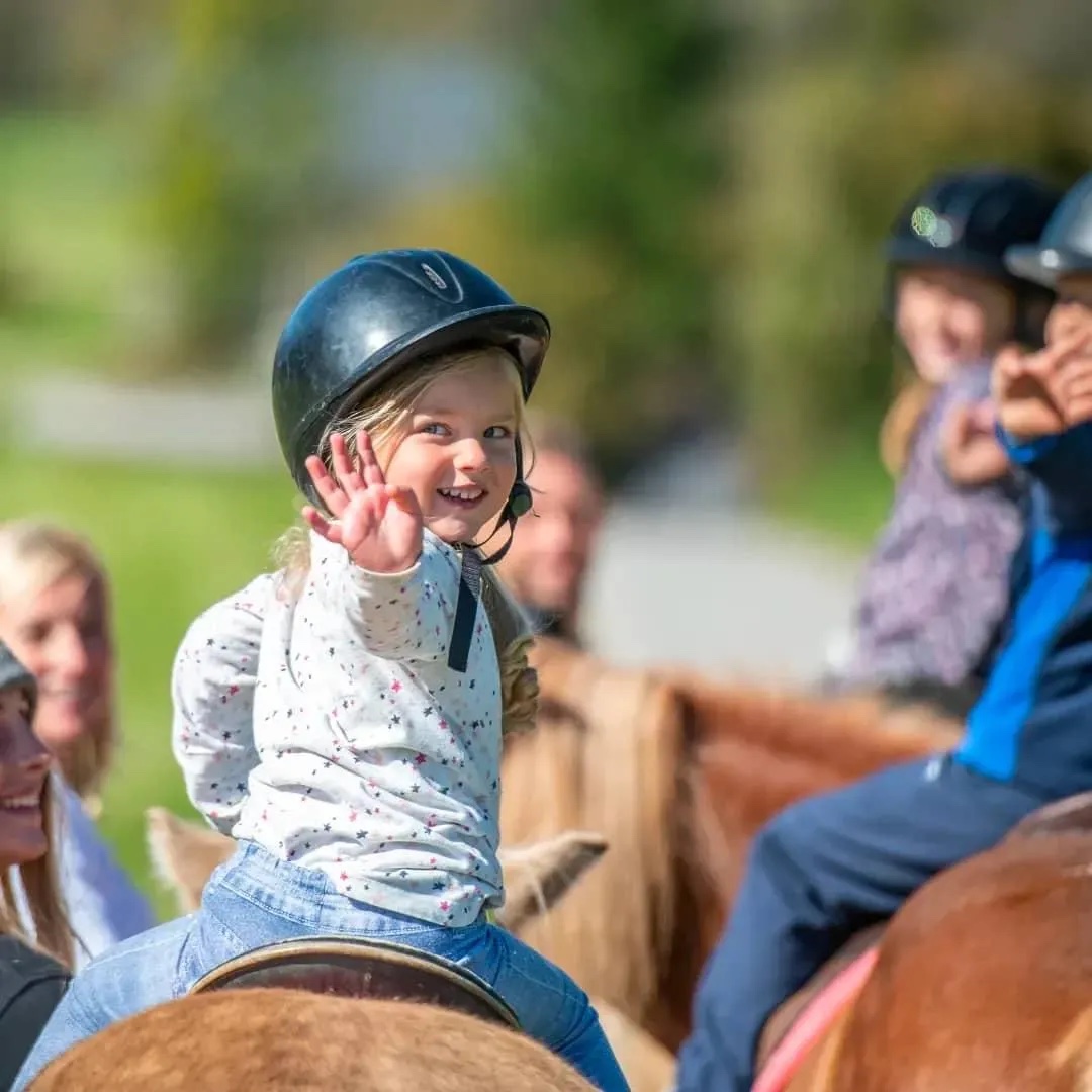 A young rider waving from her pony during a group lesson outdoors